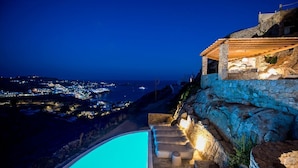 Zona de piscina con vista a un pueblo costero de noche.