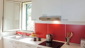 A compact kitchen with white cabinets, a red backsplash, a sink, a stove, an oven, and a washing machine. - Villa Arithmos - Three Bedroom Villa, Sleeps 6 (Lefkada)