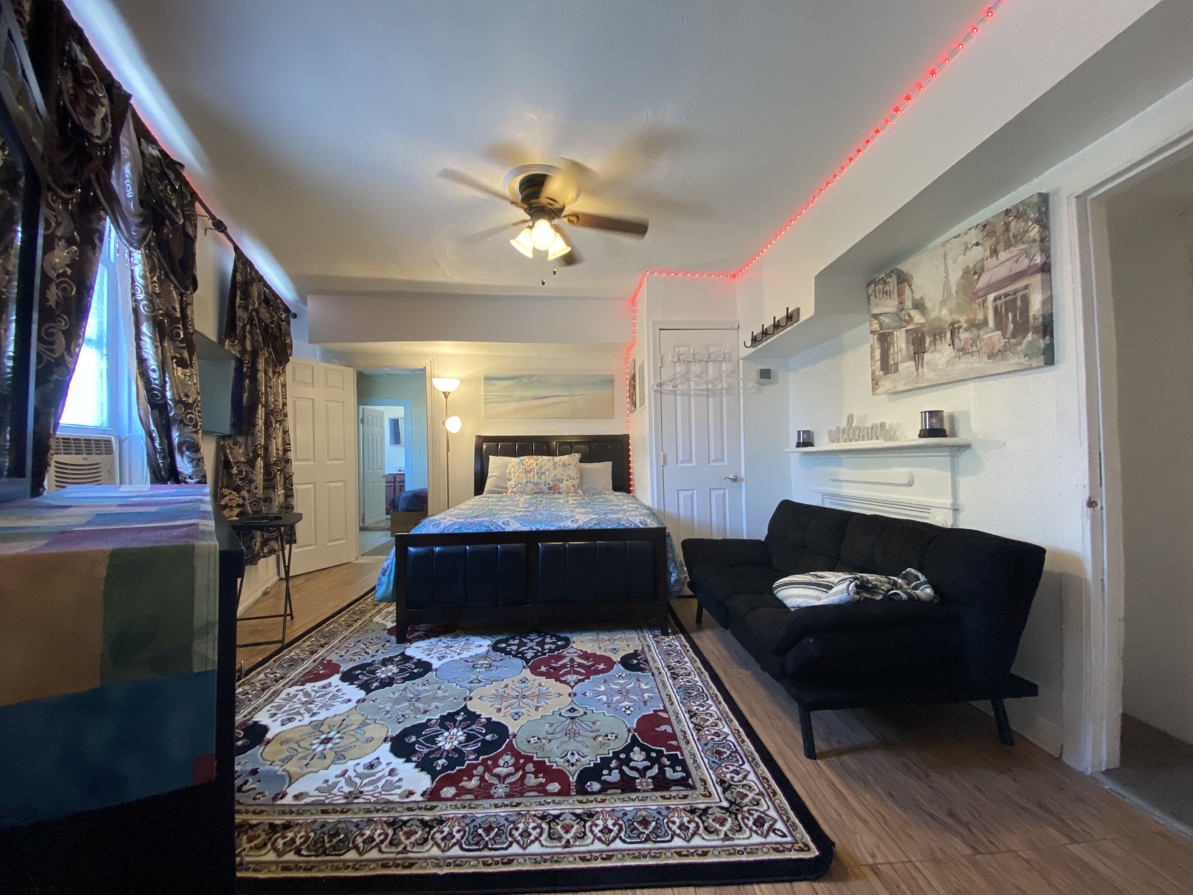 A bedroom with a bed, a ceiling fan, a patterned rug, a black sofa, and a fireplace.