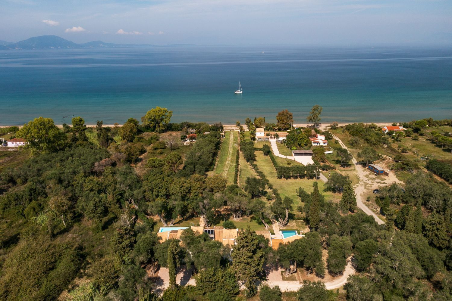 An aerial view of a coastal property with multiple houses, a swimming pool, and a boat in the distance.