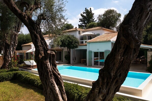 Eine moderne Villa mit Swimmingpool, umgeben von hohen Bäumen und einem gepflegten Garten.