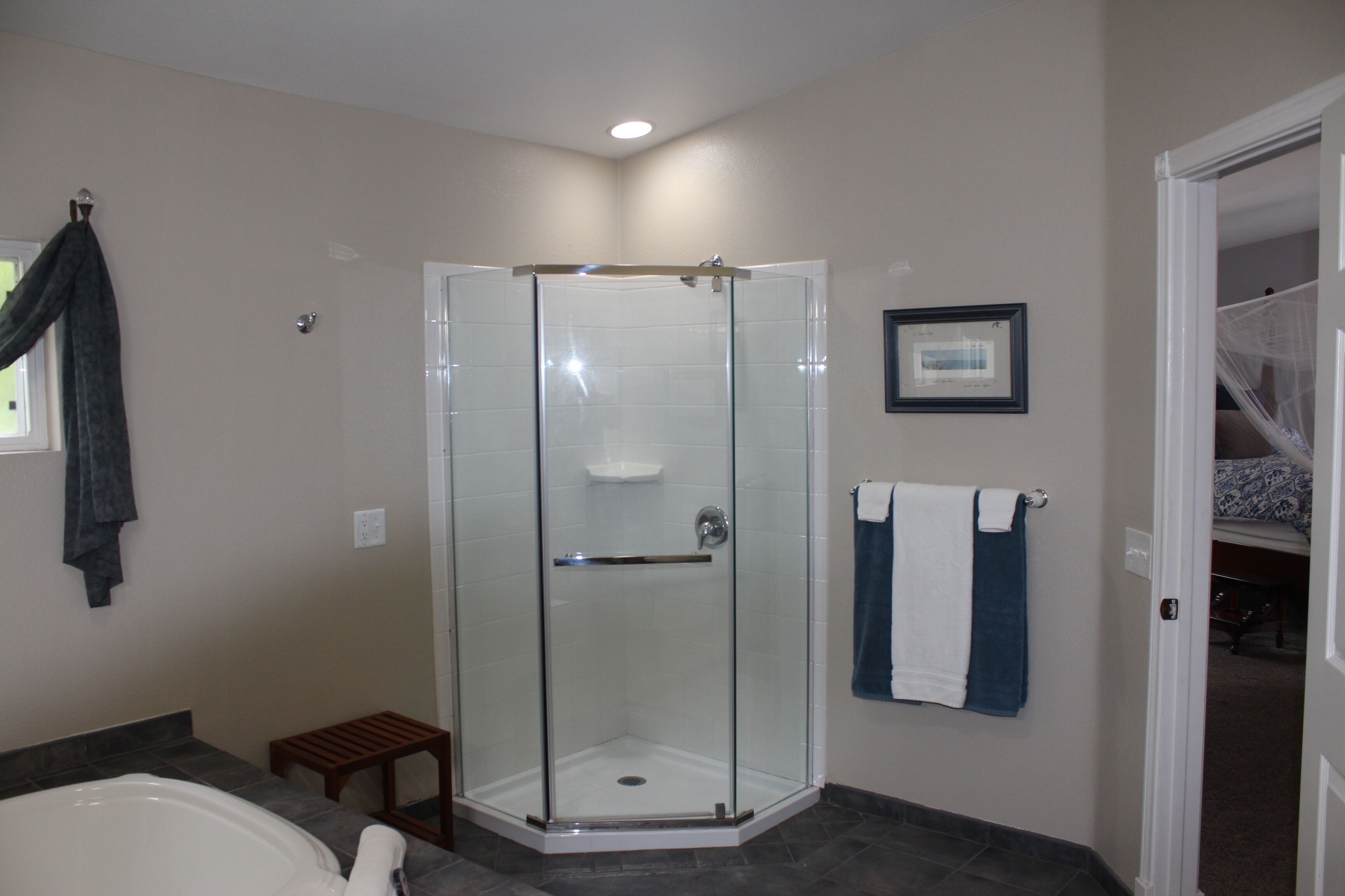 A modern bathroom with a glass-enclosed shower, a bathtub, and a small wooden stool.