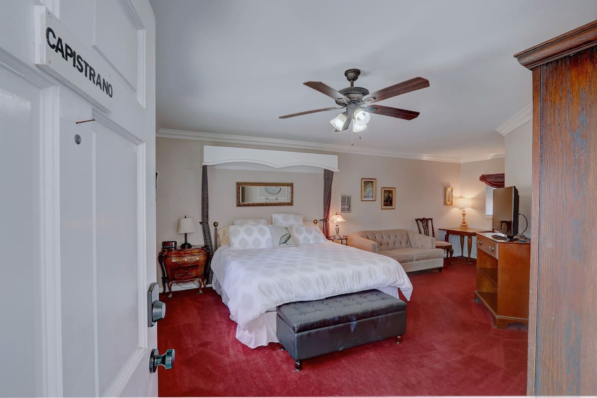 A bedroom with a bed, a ceiling fan, a dresser, and a door labeled "CAPISTRANO".