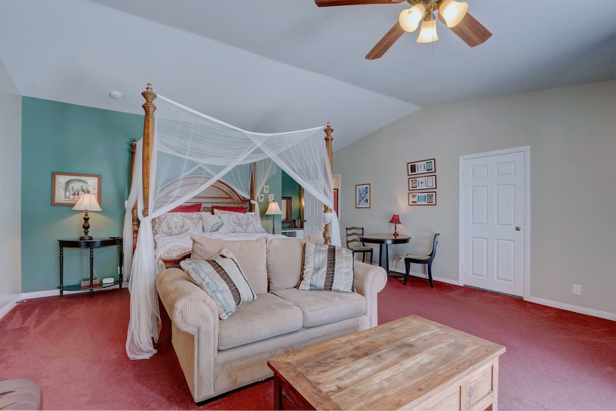 A bedroom with a four-poster bed, a wooden coffee table, a sofa, and a chair.