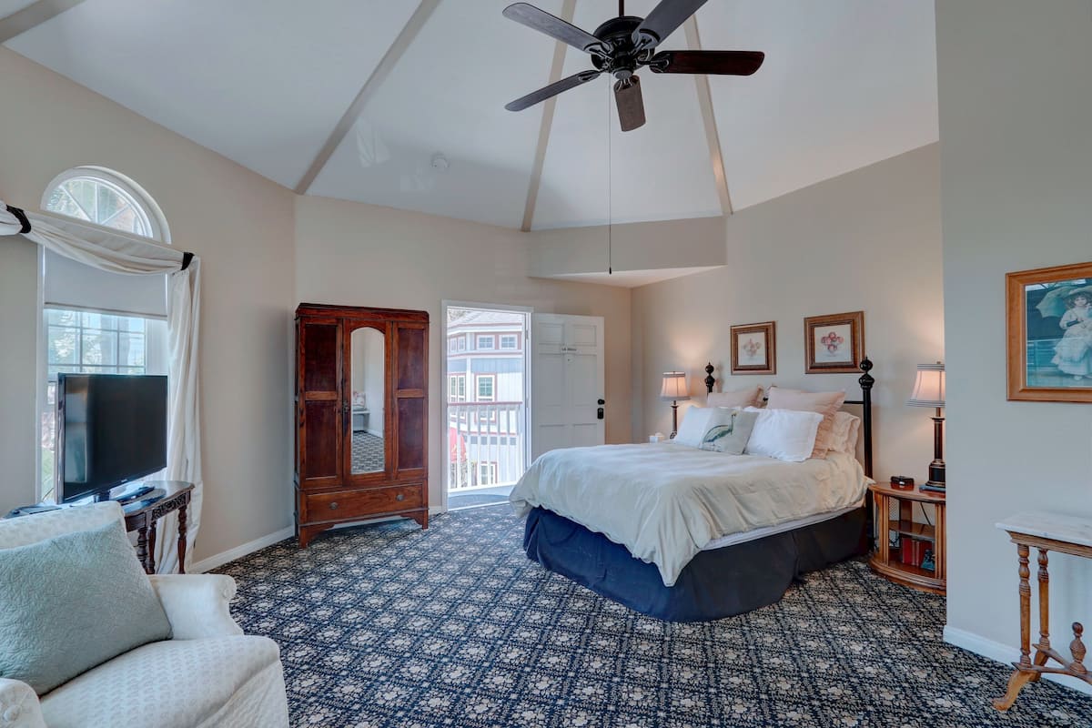 A bedroom with a large bed, a ceiling fan, a TV, and a window with curtains.