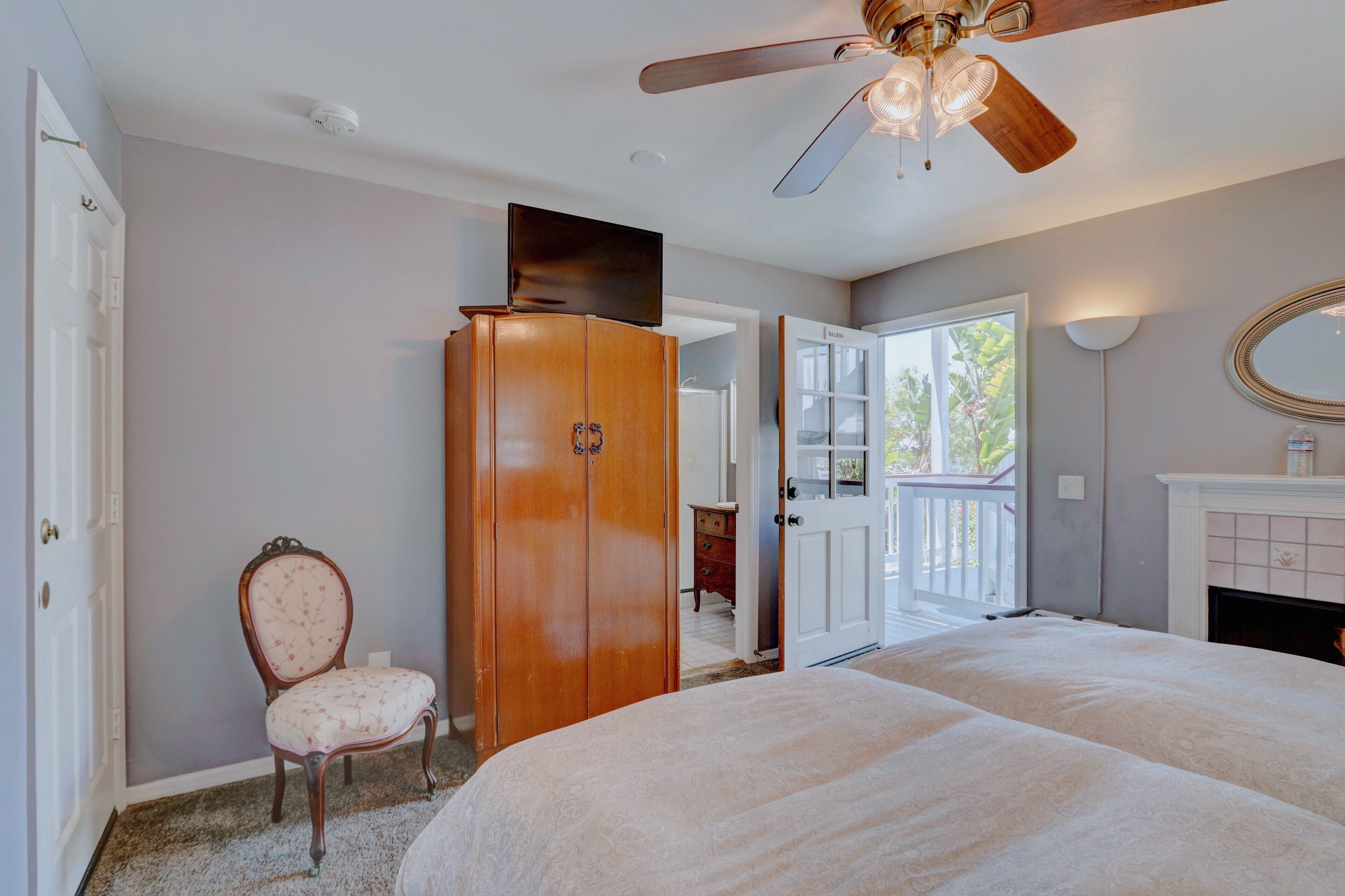 A bedroom with a bed, a wardrobe, a chair, a ceiling fan, and a fireplace.