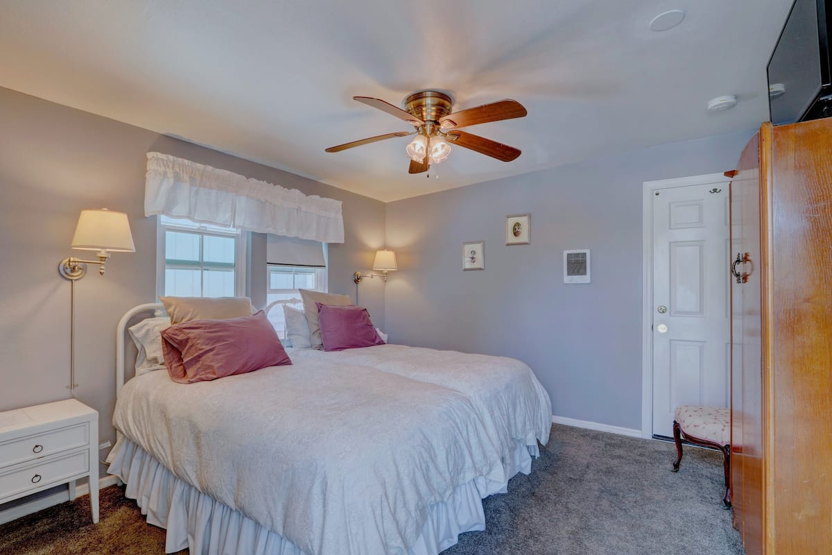 A bedroom with a bed, bedside lamps, a ceiling fan, a door, and a chair.