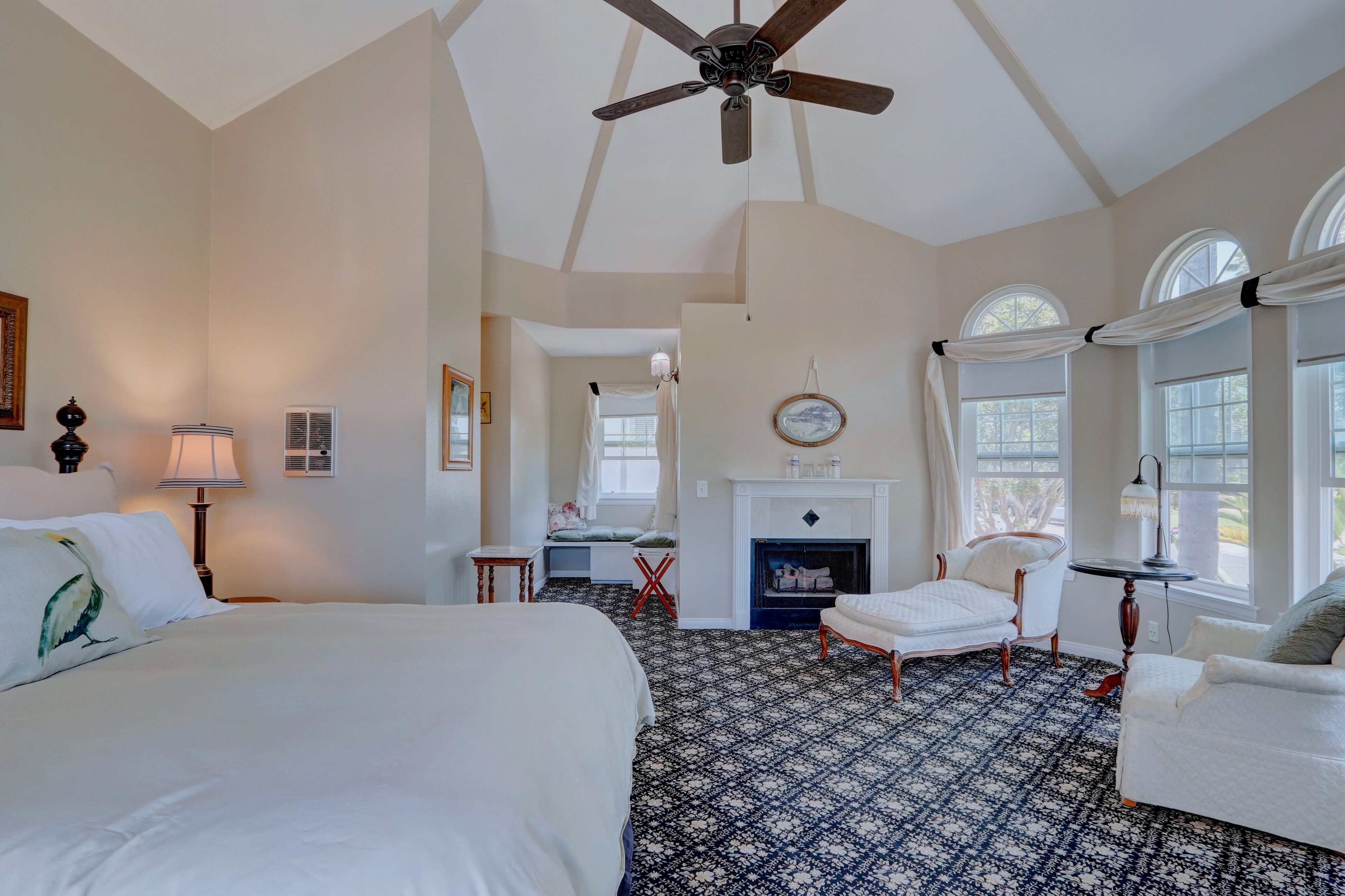 A spacious bedroom with a large bed, a desk, a fireplace, and a seating area with a chair and a sofa.
