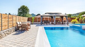 Une piscine avec une terrasse en bois, du mobilier d’extérieur et un espace salon abrité.