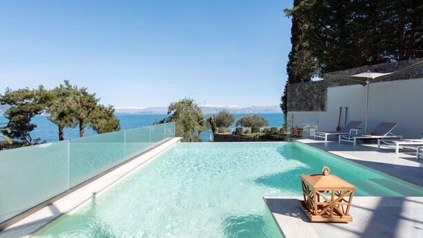 A rectangular swimming pool with clear water, surrounded by a glass barrier, and overlooking a body of water with trees and a clear sky. - Villa Chloris - Three Bedroom Villa, Sleeps 8 (Kontokali)