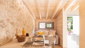 A cozy wooden cabin with a dining area featuring a table set for two, a wicker basket, and a rustic stone wall. - Villa Chloris - Three Bedroom Villa, Sleeps 8 (Kontokali)