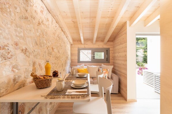 A cozy wooden cabin with a dining area featuring a table set for two, a wicker basket, and a rustic stone wall.