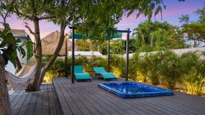 Une terrasse en bois avec un jacuzzi, deux chaises longues et un hamac.
