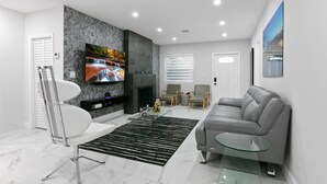 Un salon moderne avec un téléviseur à écran plat, une cheminée, un canapé gris et une table basse en verre.