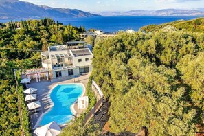 A modern hotel with a swimming pool, surrounded by lush greenery and overlooking a scenic coastline. - Villa Asteria - Five Bedroom Villa, Sleeps 12 (Limni)