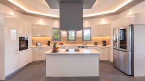 Een moderne keuken met witte kasten, een centraal eiland, roestvrijstalen apparatuur en een groot raam voor natuurlijk licht.