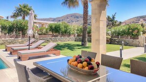Un área de comedor al aire libre con mesa de vidrio, sillas de mimbre y un frutero.