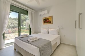 A bedroom with a bed, white curtains, an air conditioning unit, a painting, and a view of the outdoors.