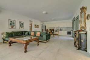 A spacious living room with a green sofa, a wooden coffee table, and a dining area with a wooden table and chairs.