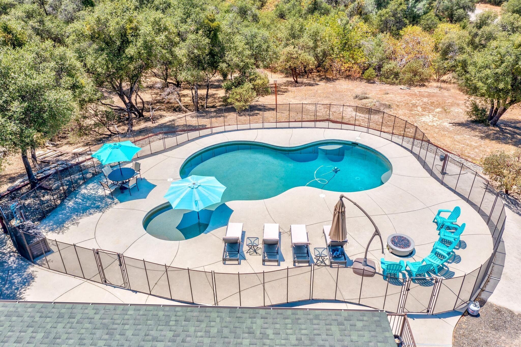 Une piscine au design incurvé, entourée d’une clôture et dotée de chaises longues et de parasols.
