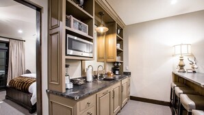 Una habitación de hotel compacta con kitchenette, una cama, baño y un pequeño rincón de descanso.