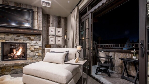 Un dormitorio con chimenea de piedra, un sofá, un televisor y un balcón con mobiliario exterior.