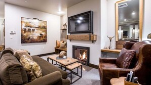 A living room with a fireplace, a television mounted above it, a sofa, a leather armchair, and a painting on the wall.