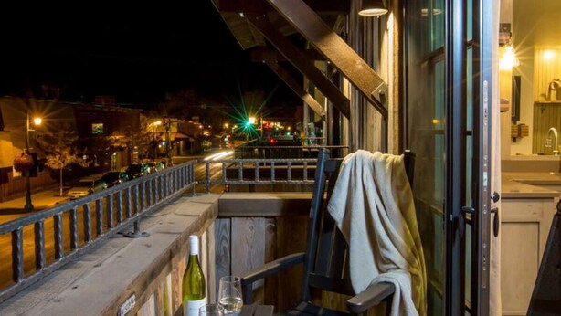 A balcony with a table, two chairs, a bottle, and glasses.