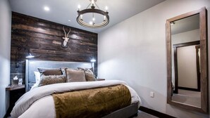 A bedroom with a wooden headboard, a chandelier, a large mirror, and a plush bed.