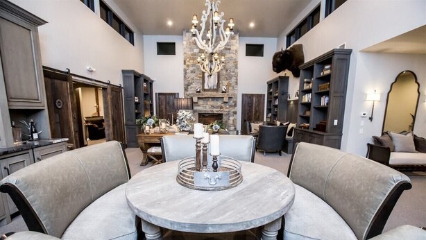 Un salón amplio con chimenea de piedra, un candelabro y una mesa de comedor redonda rodeada de sillas tapizadas.