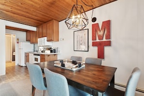 A modern kitchen with wooden cabinets, a white refrigerator, and a dining area with a dark wooden table and light blue chairs. - Waterfront, Whitefish Lake Condo, 2CD (Whitefish)