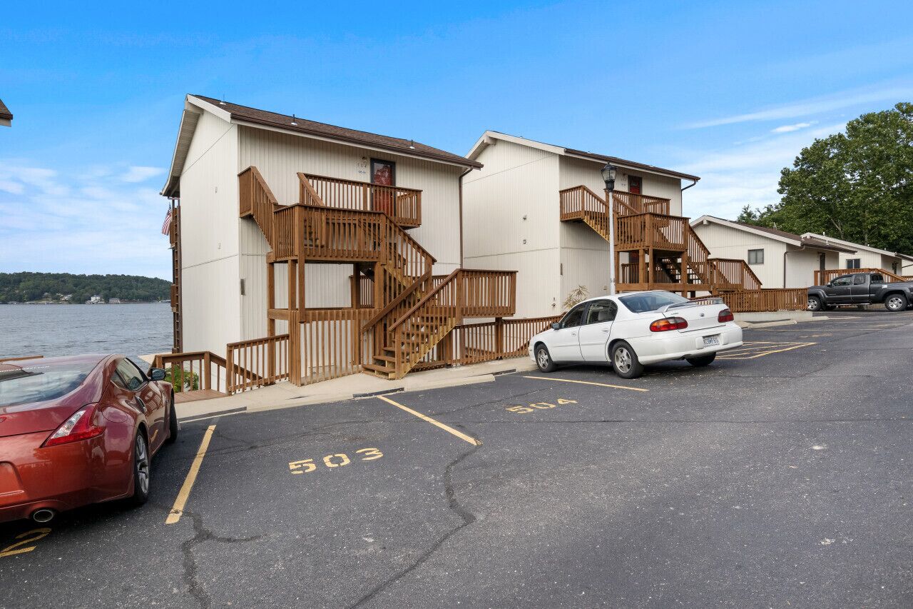 A row of motel buildings with wooden staircases and balconies, parking spaces marked 503 and 504, and a body of water in the background.