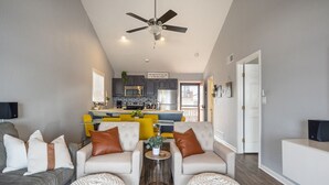 Una sala moderna con un sofá, sillones y una mesa de centro. Se ve una cocina al fondo con un comedor.