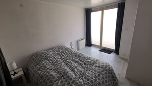 A bedroom with a large bed, a bedside table with a lamp, a radiator, and a view of the outside through a sliding door.