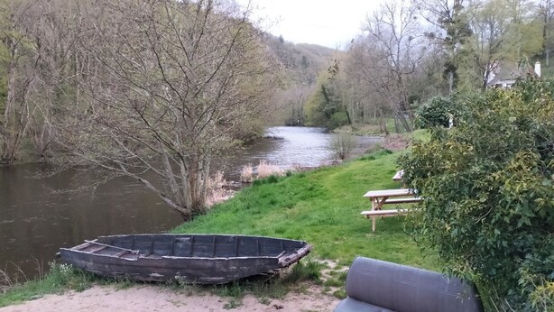 A riverside picnic area with a boat, benches, and lush greenery.