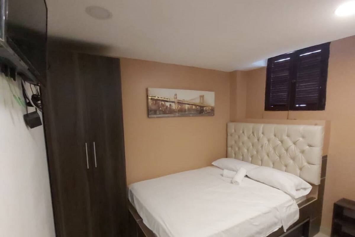 A bedroom with a bed, a wardrobe, a painting, and a window.