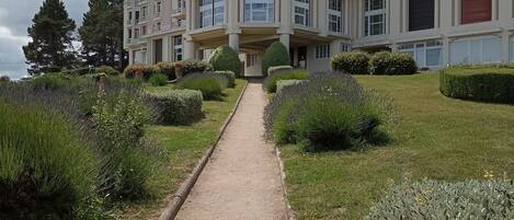 A multi-story building with a central entrance, surrounded by well-maintained gardens and a pathway leading to the entrance.