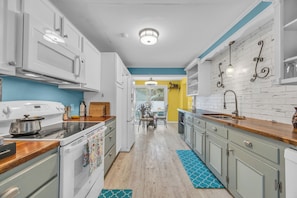 Una cocina con armarios blancos, encimera de madera y alfombra azul estampada.