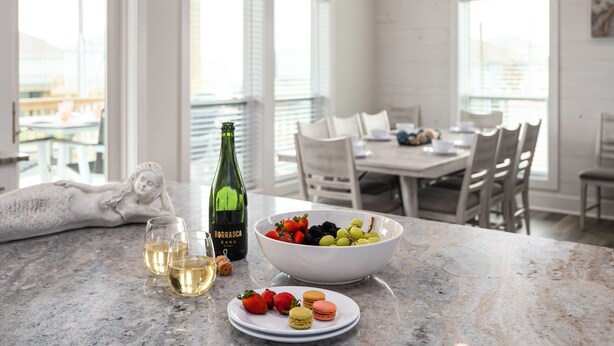 A kitchen with a marble countertop, a bowl of fruit, wine glasses, and a bottle of wine. - Brand NEW Beach House Coastal Point  (Bolivar Peninsula)