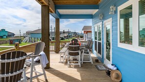 A covered deck with wooden chairs and tables, overlooking a residential area. - Brand NEW Beach House Coastal Point  (Bolivar Peninsula)
