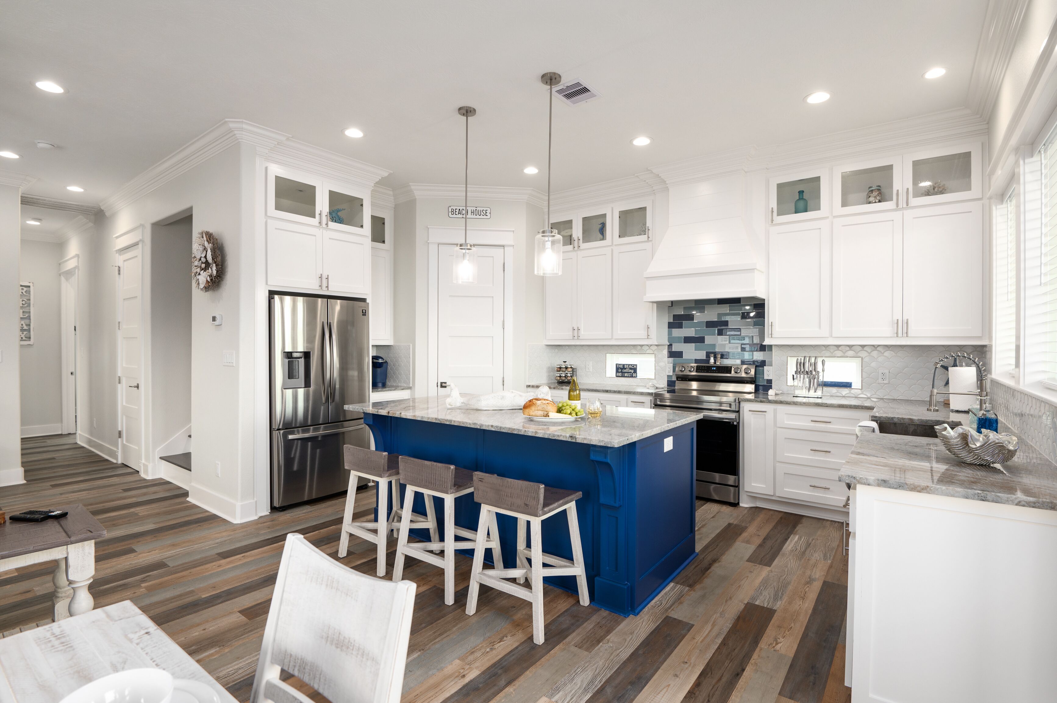 Una cocina moderna con armarios blancos, una isla azul, electrodomésticos de acero inoxidable y piso de madera.
