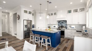 A modern kitchen with white cabinetry, a blue island, stainless steel appliances, and a herringbone wood floor. - Brand NEW Beach House Coastal Point  (Bolivar Peninsula)