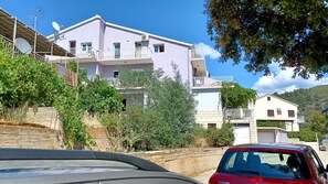 Un immeuble résidentiel doté de nombreux balcons, de plusieurs antennes paraboliques et d’une voiture garée devant.