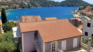 A coastal building with a tiled roof, a staircase, and a view of a bay with boats. - Bertie's Lodge - Two Bedroom Apartment with Terrace and Sea View (Smokvica)