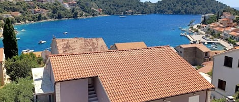 A coastal building with a tiled roof, a staircase, and a view of a bay with boats.
