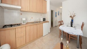 A compact kitchen with wooden cabinets, a microwave, a coffee maker, and a dining area with a table set for two. - Bertie's Lodge - Two Bedroom Apartment with Terrace and Sea View (Smokvica)