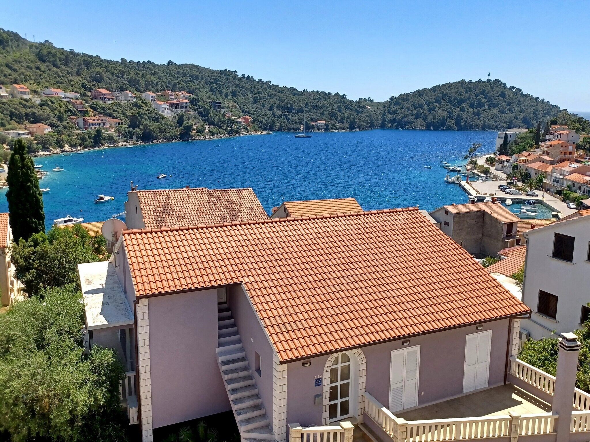 Un bâtiment situé sur la côte, doté d’un toit en tuiles, d’un escalier et offrant une vue sur une baie où se trouvent des bateaux.
