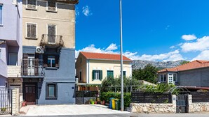 A two-story building with a balcony, a street lamp, and a mountain in the background. - Apartments Keka - Studio Apartment (Kastel Sucurac)