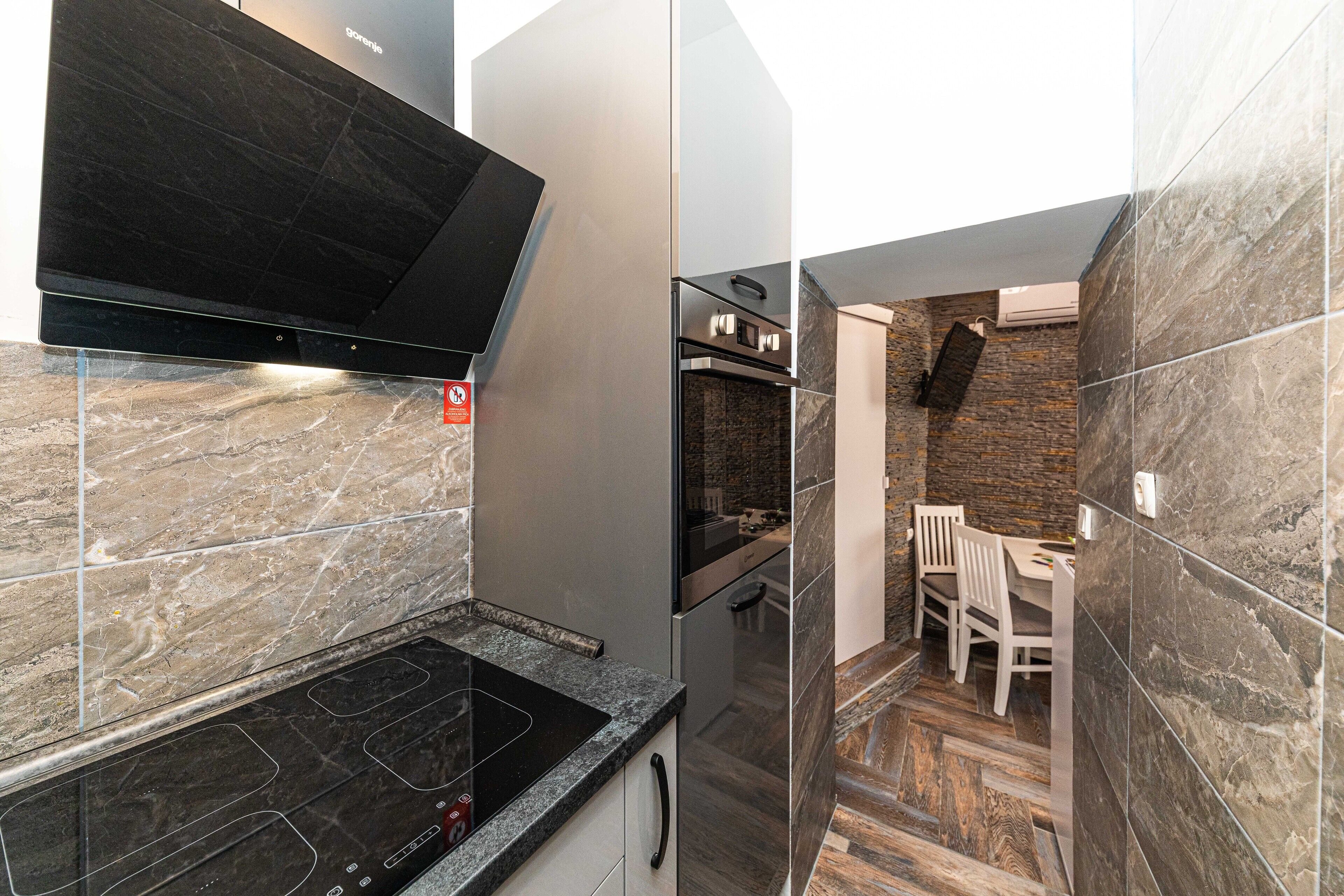 A modern kitchen with a black stove, stainless steel appliances, and a stone backsplash.