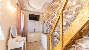 A compact kitchen with a wooden staircase, a small white cabinet, and a mirror on a white table.
